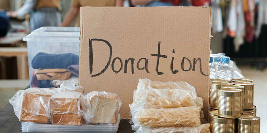 some bread, pasta, canned goods, plastic container with clothes and a cardboard with the word "Donation" written on it